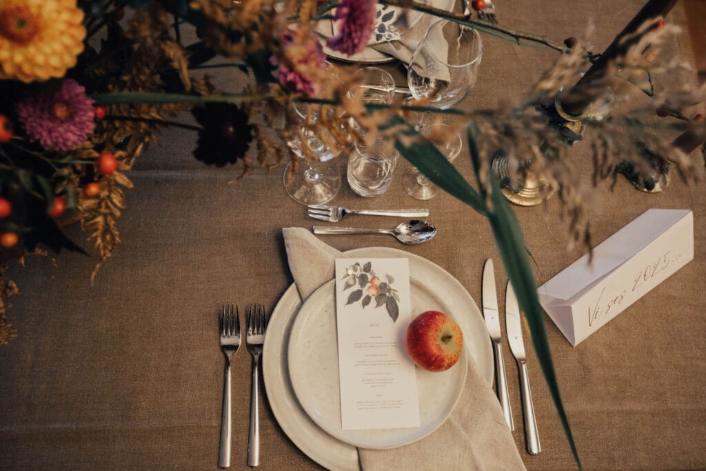 Ett dukat bord med en beige duk, blommor och ett äpple på tallriken.