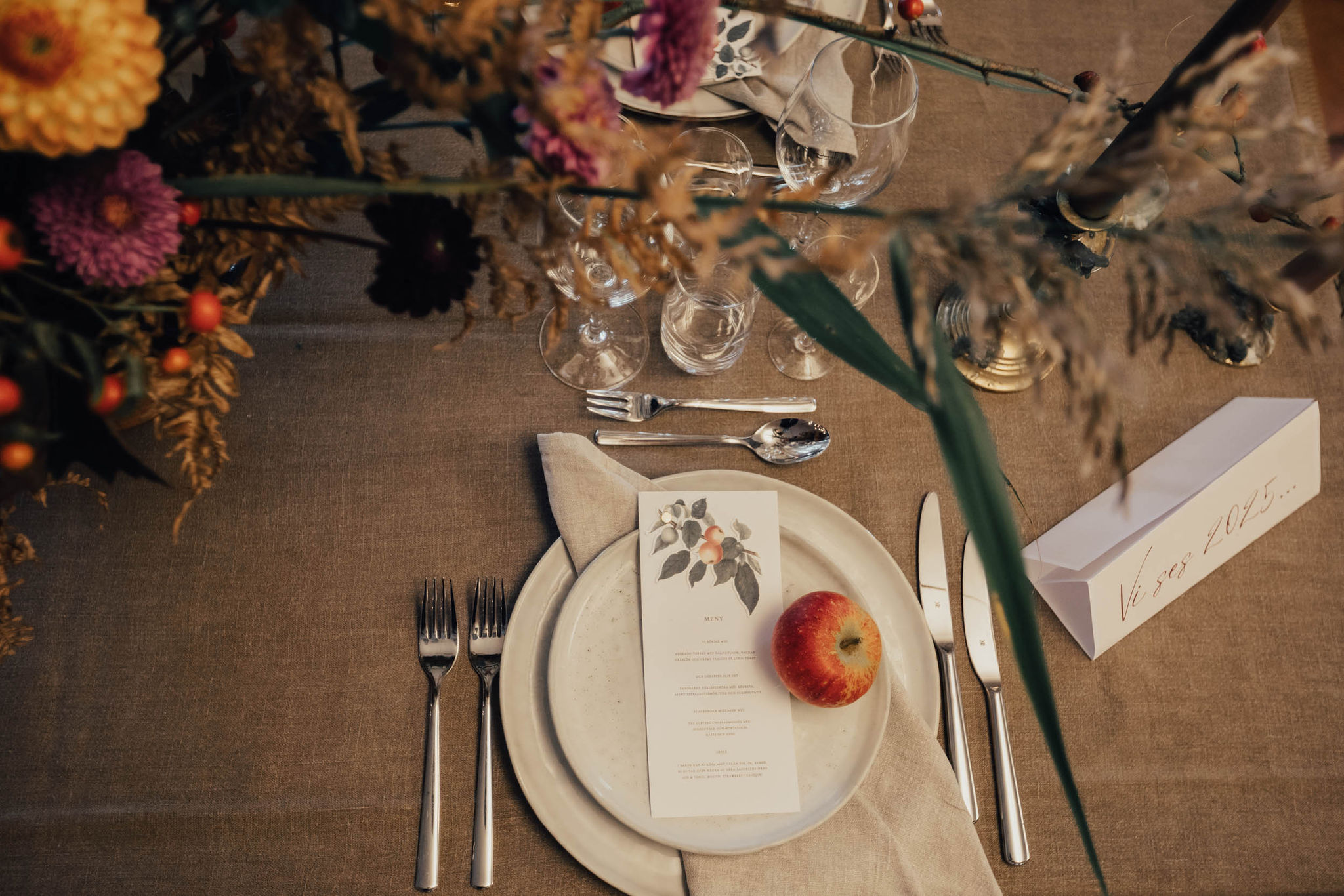 Ett dukat bord med en beige duk, blommor och ett äpple på tallriken.
